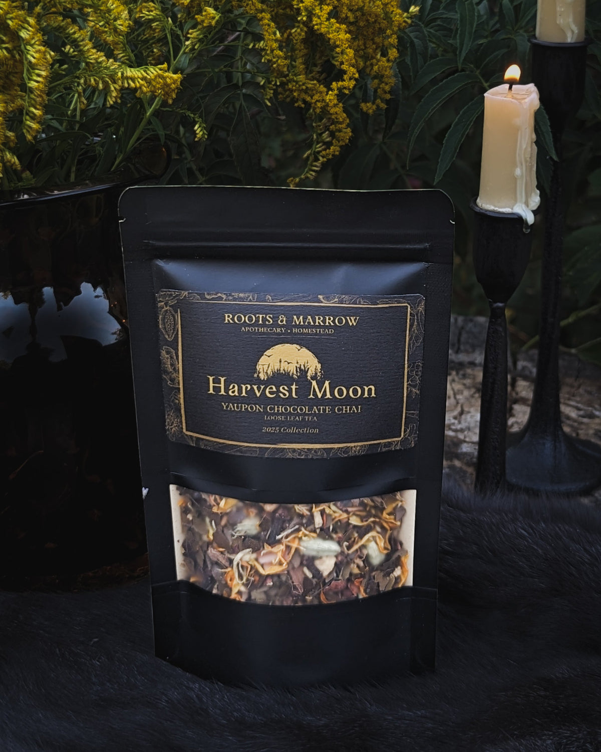 Black package of 'Harvest Moon' chocolate chips with a candle and greenery in the background. Goth tea. Gothic tea. Yaupon tea. Yaupon holly ilex vomitoria.