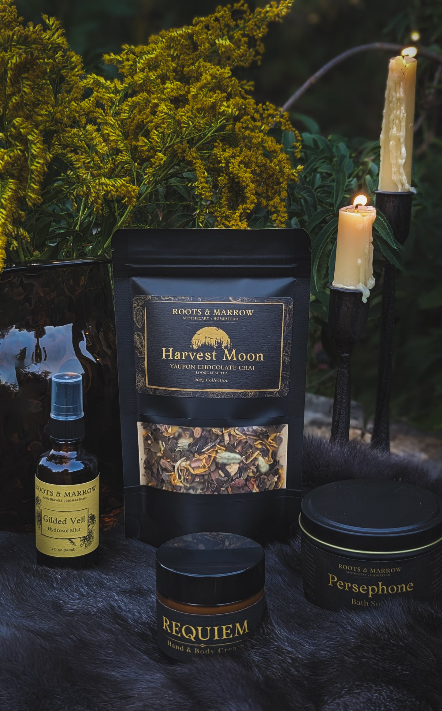 Gothic-themed products including a bottle, jar, and package on a dark surface with candles and plants. Natural skin care herbs. Natural skin care moisturizer. Gothic perfume. Goth perfume.